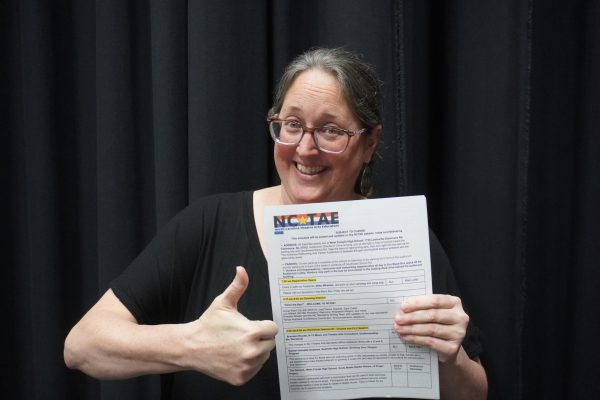 Theatre director Renae Hubbard holding NCTAE poster.